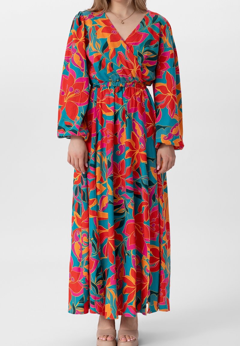 Robe longue et vibrante avec un motif floral en rouge, orange et vert. Fabriquée en tissu léger avec un design enveloppant et une taille élastique.
