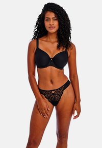 Soutien-gorge rembourré noir avec des détails en dentelle au centre et thong en dentelle noire présentant un motif floral et des accents en découpe. Texture lisse.