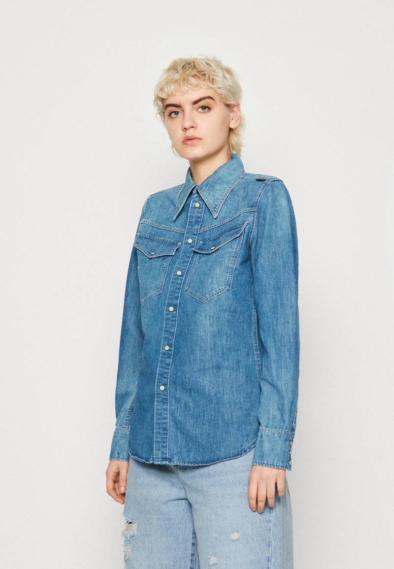 Hellblaue Denim-Hemd mit spitzem Kragen, zwei Brusttaschen und Druckknopfverschluss. Verfügt über einen leicht abgerundeten Saum und lange Ärmel.