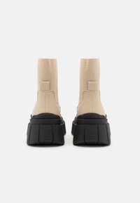 Beige ankle boots with a fitted design and large black platform heels. Smooth texture with minimal stitching and a back pull tab.