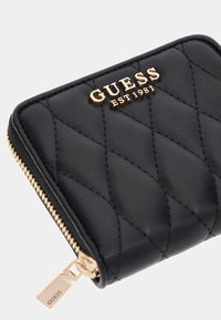 Portafoglio zip-around in pelle trapuntata nera con logo dorato "GUESS EST 1981" e zip pull coordinato in oro.