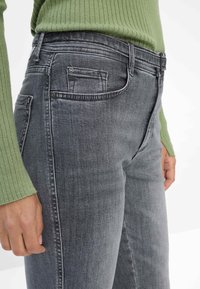 Jeans in denim grigio con vestibilità slim, dotati di un design a cinque tasche, cuciture discrete e una texture liscia. La vita include un piccolo passante.