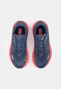 Des chaussures de course navy avec des semelles rouges présentent une tige en maille, un motif en zigzag et un logo GORE-TEX. Conception à lacets avec une semelle intermédiaire rembourrée.