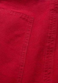 Tissu rouge à texture lisse, doté d'une poche plaquée et de détails de couture visibles. Le tissu semble robuste et tissé serré.