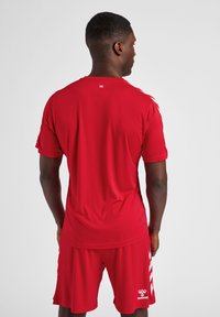 Rød sports T-shirt med korte ærmer, lavet af glat stof. Har et lille logo på ryggen og er parret med matchende røde shorts.