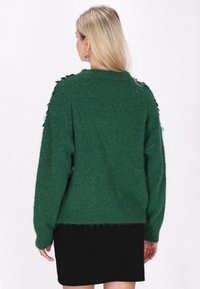 Zielony sweter z dzianiny o fakturowanym wykończeniu, z czarnymi guzikami zdobiącymi ramiona oraz luźnym krojem.