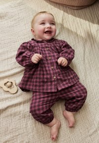 Ensemble pour bébé en tissu à carreaux violets avec fermeture à boutons, manches longues, poignets élastiques et pantalon assorti. Texture douce. Jouet en bois à proximité.