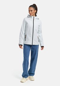 Veste bleu clair avec capuche, fermeture éclair à l'avant et accents noirs. Dotée de deux poches latérales, de manches longues et d'une coupe décontractée, associée à un jean bleu.