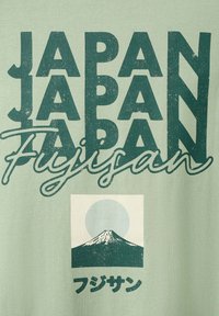 Texte « JAPAN » répété verticalement avec « Fujisan » écrit en script, accompagné d’un Mont Fuji stylisé avec un soleil derrière et des caractères japonais en dessous.