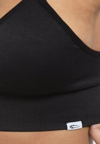 Zwarte geribbelde bralette met een strak ontwerp. Voorzien van dunne bandjes en een label aan de onderrand, wat een minimalistische esthetiek uitstraalt.