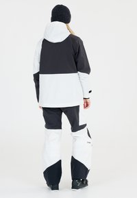 Skidjacka och byxor set i svart och vitt. Jackan har huva och färgblockdesign. Byxorna har vida ben och distinkta mönster.