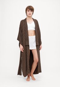 Robe kimono à motifs marron en tissu léger, avec un ajustement ample et un design à devant ouvert. Porté sur un crop top blanc et un short.