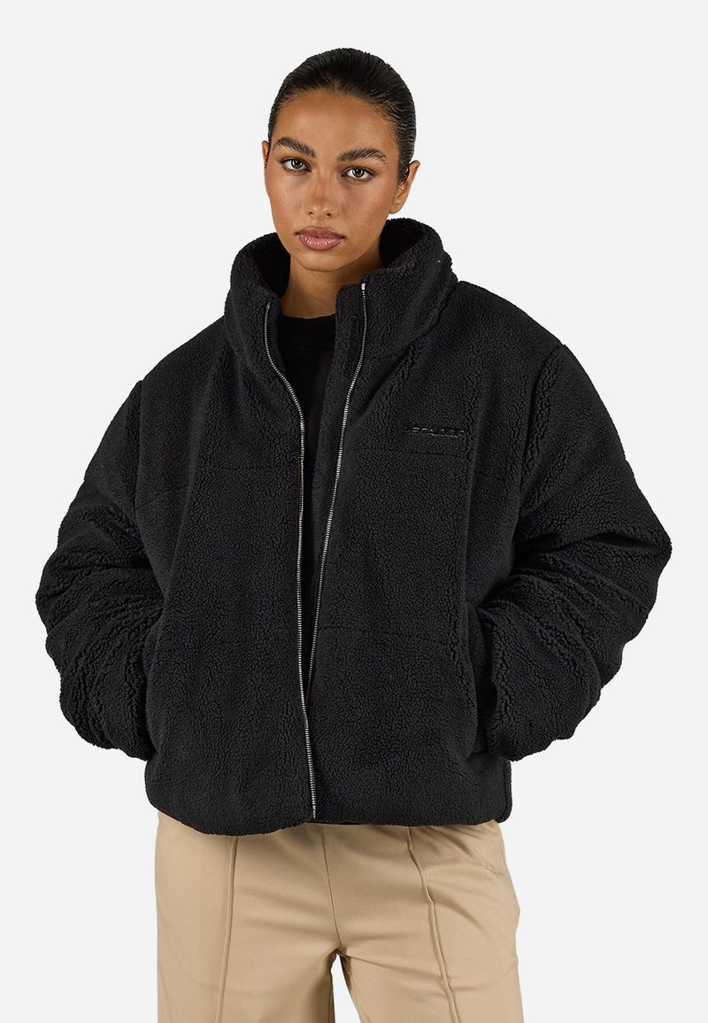 Giacca in pile nera con colletto alto, chiusura con zip e superficie texturizzata. Presenta un logo minimalista ricamato sul davanti.