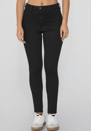Černé skinny džíny vyrobené z denimu, s vysokým pasem, disponující zapínáním na knoflík a předními kapsami. V kombinaci s bílými teniskami.