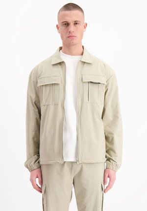 Light khaki jacket with a zip front, two chest pockets, and elastic cuffs. Made of soft fabric with a relaxed fit.