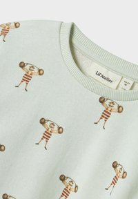 Heledad roheline toddleri särk, millel on korduv muster vintage tugevmeestest, kes tõstavad baaritalasid, ümmargune kaelus ja Lil'Atelier sildiga sees.