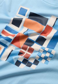 Light blue T-shirt featuring a colorful abstract geometric design with various squares in shades of blue, orange, and navy.