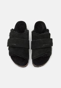 Black suede sandals feature cross straps, a soft fuzzy lining, and a contoured footbed. Minimalist design with no visible hardware.