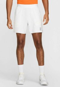 Shorts sportivi bianchi con elastico in vita, due tasche laterali e un piccolo logo. Indossati con calze bianche e sneakers.