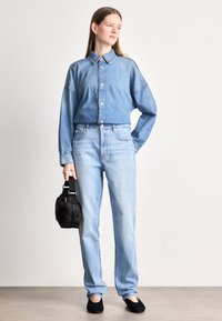 Denim srajca s gumbi v svetlo modri barvi, z ovratnikom in spuščenimi rameni; kombinirana z svetlo modrimi hlačami z višjim pasom in črno torbico.