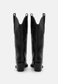 Czarne skórzane kowbojki z ostro zakończonym czubkiem, gładkim wykończeniem i kontrastującymi przeszyciami po bokach. Kwadratowe obcasy i pętle do łatwego zakładania.