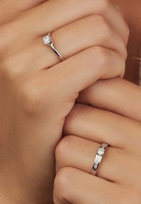 Des bagues en argent présentent un bandeau texturé et des pierres précieuses transparentes, l'une avec une pierre centrale proéminente et l'autre avec plusieurs petites pierres.