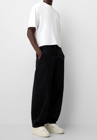 White short-sleeve t-shirt paired with loose-fitting black jeans and cream sneakers. The outfit has a casual, relaxed fit.