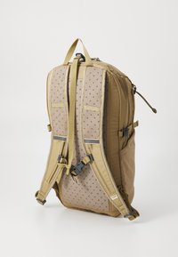 Tan backpack featuring padded mesh back for comfort, adjustable straps, and side pockets. Durable fabric with a structured design.
