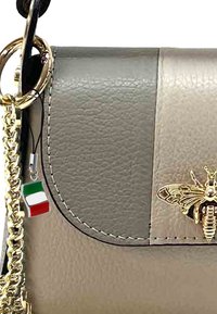 Leren handtas met een tweekleurig ontwerp in grijs en beige. Inclusief een gouden kettingriem en een decoratieve bij en vlag charm.