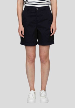 Shorts bleu marine avec fermeture à bouton, avec revers et poches latérales. Associés à des baskets blanches et un haut rayé.