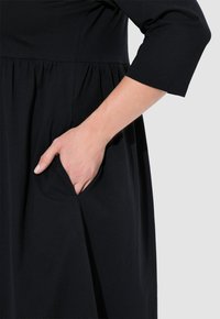 Czarna sukienka z rękawami o długości 3/4 i marszczoną talią, z bocznymi kieszeniami i miękką, gładką fakturą materiału.