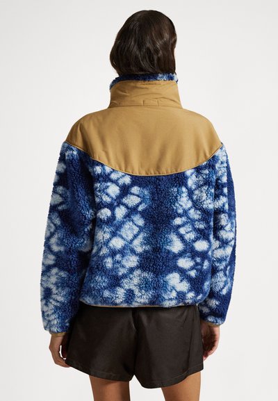 Φλις τζάκετ με μπλε μοτίβο tie-dye και ταμπά ώμους, με ψηλό γιακά και υφή απαλή και ανάγλυφη. Κατάλληλο για καθημερινή χρήση.