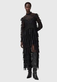 Svart spetsklänning med lager av rufser, långa genomskinliga ärmar och hög halsringning. Matchad med knähöga svarta stövlar, vilket framhäver de genomskinliga lagren.