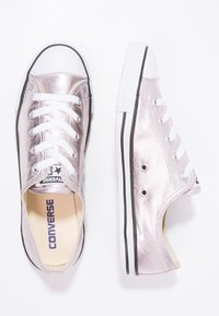 Stříbrné kovové plátěné tenisky s bílými tkaničkami a gumovými podešvemi. Disponují klasickým designem, kulatou špičkou a černými akcenty na podešvi.