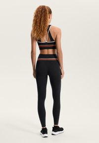 Crni sportski kratki top s bijelim i tamnocrvenim prugama, u kombinaciji s visokim crnim tajicama. Model nosi crne tenisice.