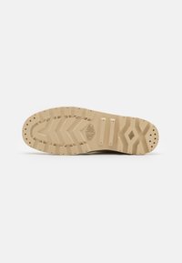 Suela de zapatilla de goma beige con un patrón texturizado, que presenta costillas y agarres circulares para tracción. Logo grabado en el costado.