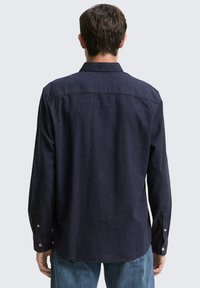 Marinefarbener Langarmshirt mit leichter Textur, Knopfmanschetten und subtilen gesprenkelten Details; klassischer Kragen und abgerundeter Saum am Rücken.