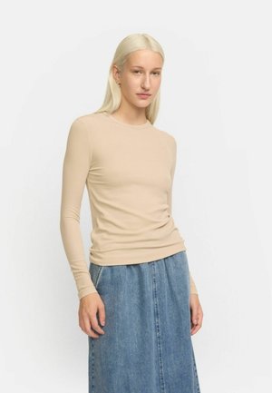 Beige Langarmoberteil mit rundem Hals, taillierter Form und gerippter Textur, kombiniert mit einem hellblauen Jeansrock in Kniehöhe.