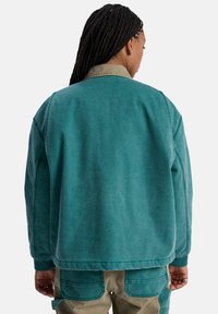 Teal bomk jacket met een contrasterende beige kraag, zachte katoenen textuur, ribbelmanchetten en een relaxte pasvorm. Zichtbare stikseldetails op de achterkant.
