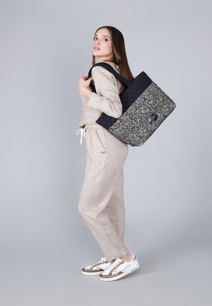 Borsa a tracolla trapuntata in bianco e nero a zigzag con manici robusti, indossata su una spalla da un modello. Design leggero e tessuto texturizzato.