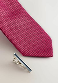 Rote gemusterte Seidenkrawatte mit einer Diamantwebe neben einer silbernen Krawattennadel mit einem horizontalen blauen Emaille-Streifen.