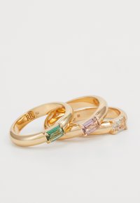 Tres anillos de oro con engastes de piedras rectangulares; uno tiene una piedra verde, otro una rosa y el tercero una piedra transparente. Bandas suaves y pulidas con un acabado brillante.