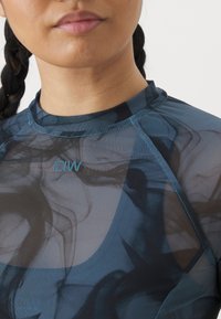 Haut de sport bleu transparent avec un col rond, présentant un motif abstrait fluide et un logo discret. Texture lisse et coupe ajustée.