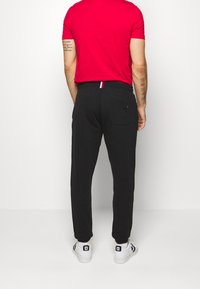 Schwarze Jogginghose mit lockerem Schnitt, ausgestattet mit einer Gesäßtasche und einem farbigen Streifen am Bund. Kombiniert mit einem roten T-Shirt und weißen Turnschuhen.