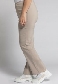 Beige, kroppsnära byxor med en slät tygtextur, lätt utsvängd nederdel och midjehöjd. Matchas med vita klumpiga sneakers.