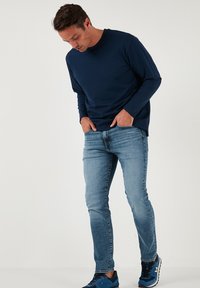 Camicia blu navy a maniche lunghe abbinata a jeans azzurri. L'outfit presenta una vestibilità comoda ed è completato da sneaker blu.