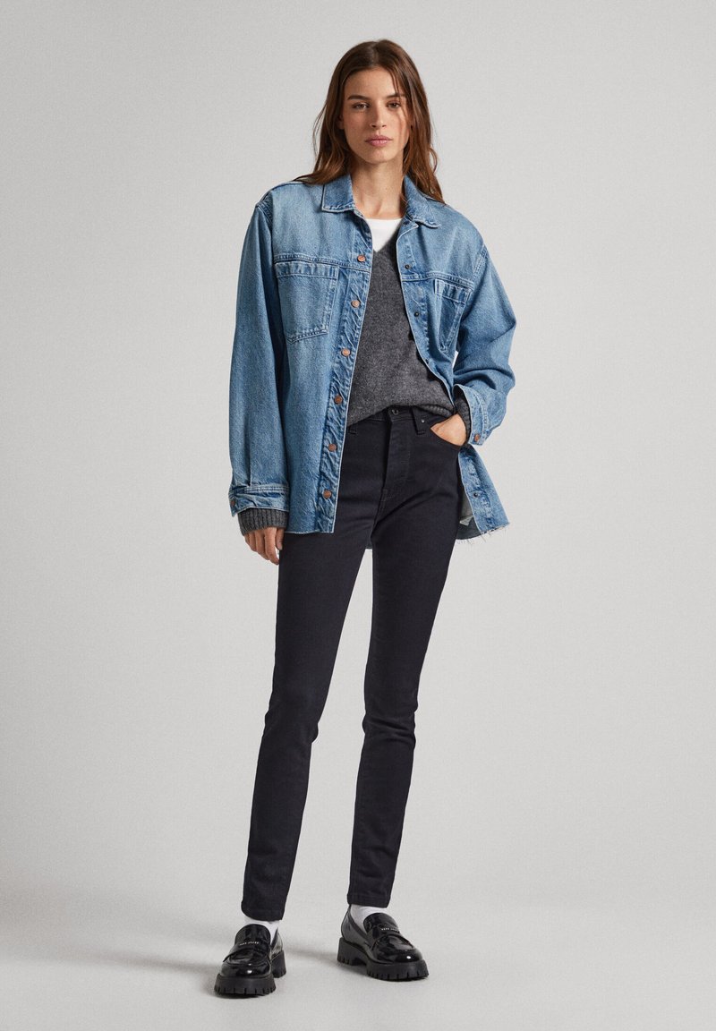 Jeansjacke in Hellblau, oversized Passform, mit Knopfverschluss und Brusttaschen. Über einem grauen Pullover und schwarzen Skinny-Jeans getragen. Schwarze Schuhe.