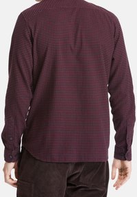 Camicia a maniche lunghe a quadri in bordeaux scuro e blu navy. Presenta un colletto classico, polsini con bottone e un orlo curvo. Tessuto texture.