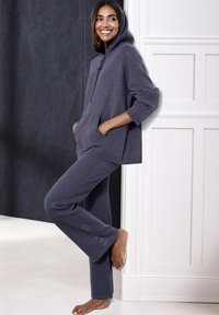 Dunkelgrauer, strukturierter Hoodie mit einer Fronttasche und einer Kapuze mit Kordelzug, kombiniert mit passenden Jogginghosen, die ein Logo am Bein haben.