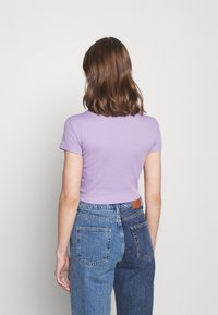 Kortärmad lila ribbad topp i kombination med tvåfärgad blå denimjeans, med en läderpatch på midjebandet och tydliga sömmar på fickorna.